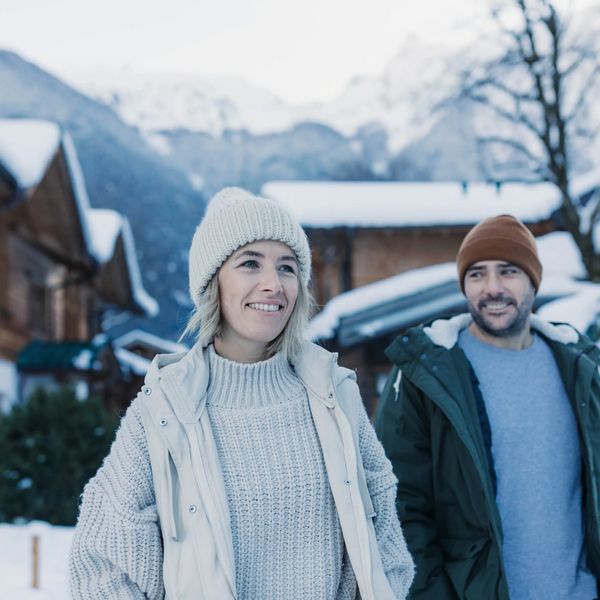 Ein Paar mit Winterbekleidung umarmt sich vor den Holz-Chalets im Feelfree Nature Resort im Winter