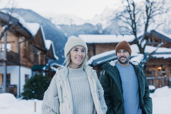 Ein Paar mit Winterbekleidung umarmt sich vor den Holz-Chalets im Feelfree Nature Resort im Winter